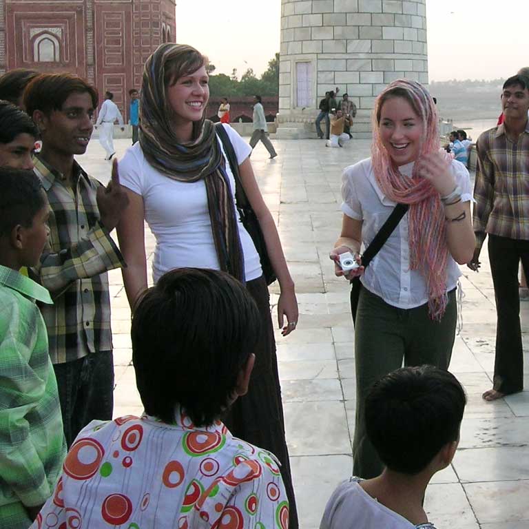 Two female students talk with young children in India