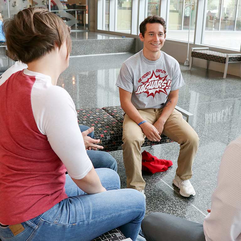A male student sits and smiles with a group of friends in the campus center.